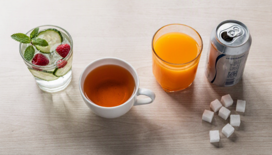 Links Wasser mit Gurke und Minze sowie ungesüßter Tee, rechts Saft, Cola und Energydrink mit Zuckerwürfeln. Auch Drinks gehören zu Lebensmitteln zum Abnehmen.