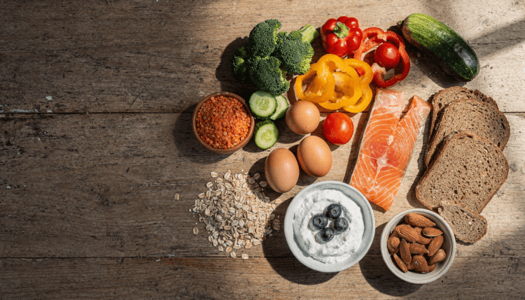 Gemüse, Hülsenfrüchte, Eier, Fisch und Vollkorn auf einem Holztisch.