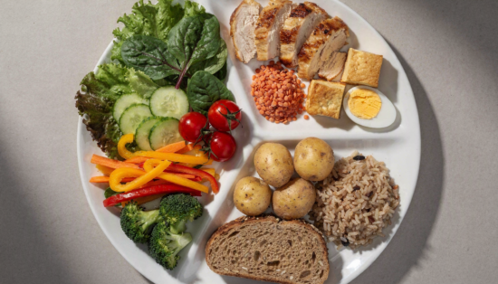 Teller nach dem DGE-Teller-Modell: Die Hälfte Gemüse und Salat, oben rechts Hähnchen, Linsen, Tofu und Ei als Eiweiß, unten rechts Kartoffeln, Vollkornreis und Vollkornbrot als Kohlenhydrate